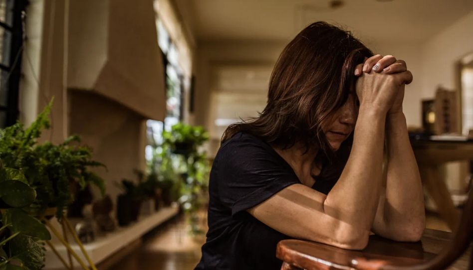 mulher orando ajoelhada na cozinha de sua casa.