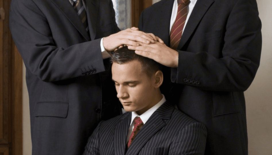Homens impondo as mãos na cabeça de outro homem para lhe conceder o sacerdócio.